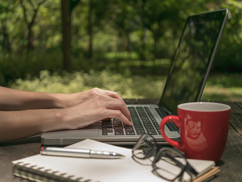 Woman using on laptop computer with red coffee cup on the vintage wooden desk in the park Working with Linda, Credentials, Coach, Organizational Change